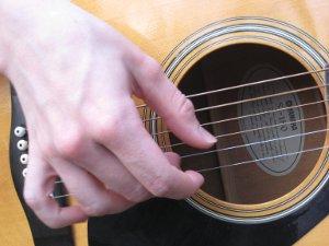 Lähikuvassa sormet näppäilevät akustista kitaraa.